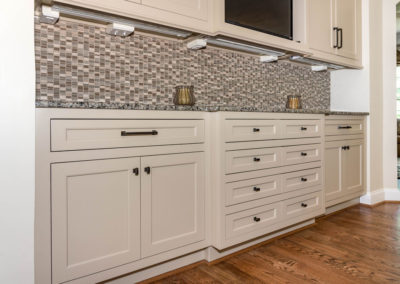 Kitchen renovation detail of sideboard custom cabinetry with flush-set doors and drawers, granite countertop, mosaic backsplash, under-cabinet recepticles and switches, and hardwood floors..