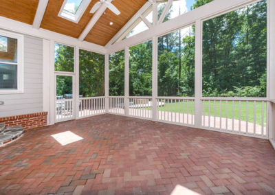 Porch renovation with custom screening, vaulted ceiling, recessed lights, faux beams, skylights, gable pediment design, and handrail on existing herringbone brick patio.