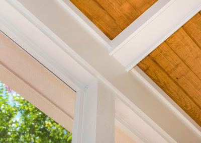 Porch renovation detail of white trimwork, tongue and groove vaulted ceiling, faux beams, and contrasting colors.