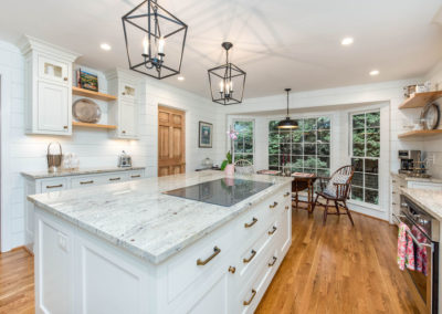 Modern farmhouse kitchen renovation with view of island, glass cooktop, flush-set custom cabinetry, antique brass hardware, shiplap wall treatment, open-frame farmhouse light fixtures, and hardwood floors.