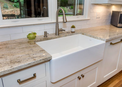 Modern farmhouse kitchen renovation detail of extra-large farmhouse sink, brushed nickel fixture, granite countertop, and flush-set custom cabinetry.