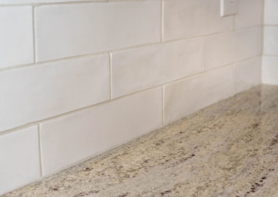 Modern farmhouse kitchen renovation detail of granite countertop and wavy white subway tile.