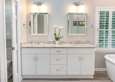 Master bath renovation has white Milan-style double vanity with granite top, three center drawers and double-doors below each sink, chrome fixtures, bevel-framed mirrors, and chrome wall fixtures.