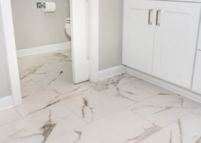 Master bath renovation detail of 12x24 marble tile floor, water closet pocket door, and vanity.