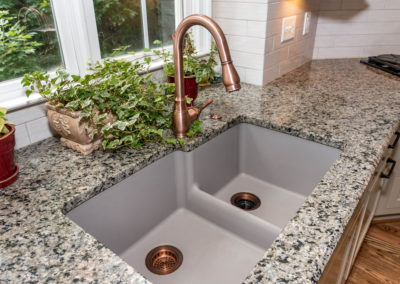Kitchen renovation detail of extra-large, inset double sink, with copper fixture and drains and granite countertop.