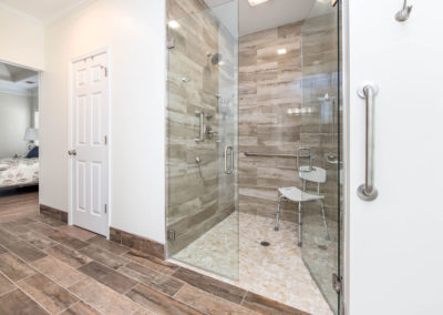 ADA-compliant master bath renovation, with curbless shower, double-swing glass doors for 4'6" opening, grab bars, hand-held sprayer, pebble tile shower pan, wood-look plank floor.