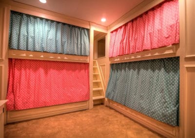 Basement renovation detail of curtained princess bunkbeds, with custom cabinetry, pull-out trundle beds, and tiny stairwell.