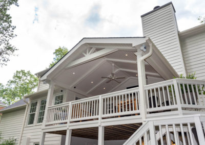 Porch renovation with view from yard of railings, crowned corner posts, vaulted tongue and groove ceiling, recessed lighting, expose beams, and custom gable pediment design.
