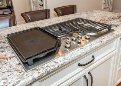 Kitchen renovation detail of natural gas island cooktop with five burners and griddle; granite countertop.