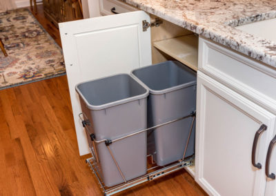 Kitchen renovation detail of under-counter pull-out trash and recycling bins in stainless steel rack.