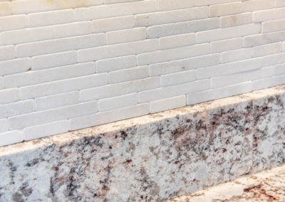 Kitchen renovation detail of granite countertop and white natural tumbled stone mosaic tile