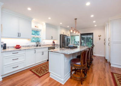 Kitchen renovation with view of island and outer wall, with granite countertop, hardwood floors, white custom cabinets, copper lighting fixture, recessed lighting, crown molding, and island stovetop