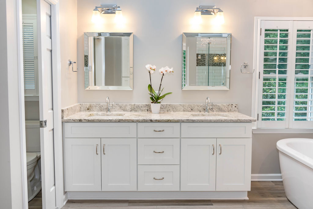 Master bath renovation has white Milan-style double vanity with granite top, three center drawers and double-doors below each sink, chrome fixtures, bevel-framed mirrors, and chrome wall fixtures.