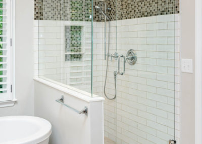Master bath renovation has glass-wall shower with wavy subway tile, mosaic tile band, wall niche, hand-held sprayer, and all-chrome fixtures